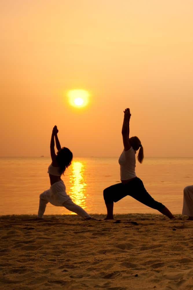 Twp girls doing yoga at sunset on the beach