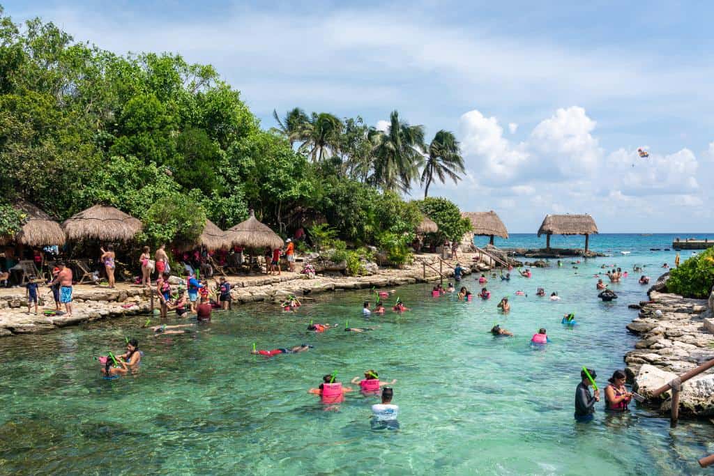 Wide, clear channel surrounded by rocks and trees with many people swimming and snorkeling
