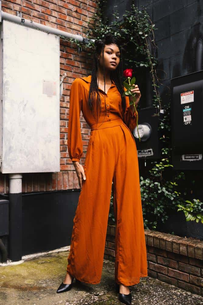 Girl in a burnt orange romper holding a rose in a small courtyard