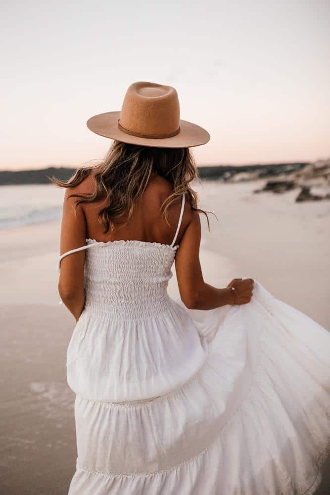 Girl in a maxi white dress with a sunhat on the beach