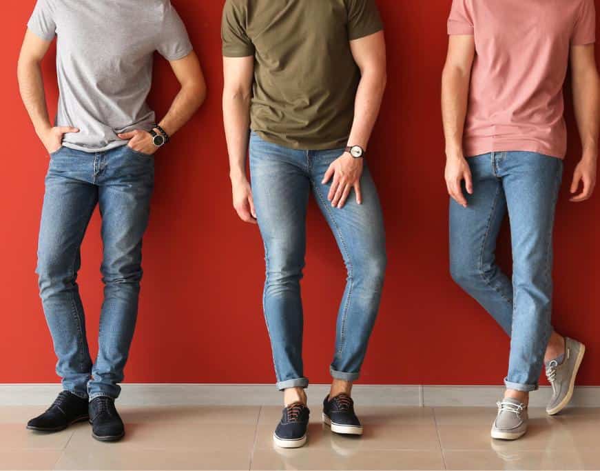 3 men in varying colored t-shits, jeans, and boat shoes against a red wall