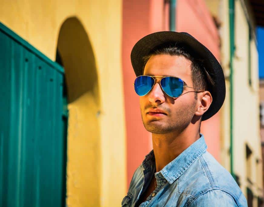Man in sunglasses, jean hat, and hat near colorful buildings