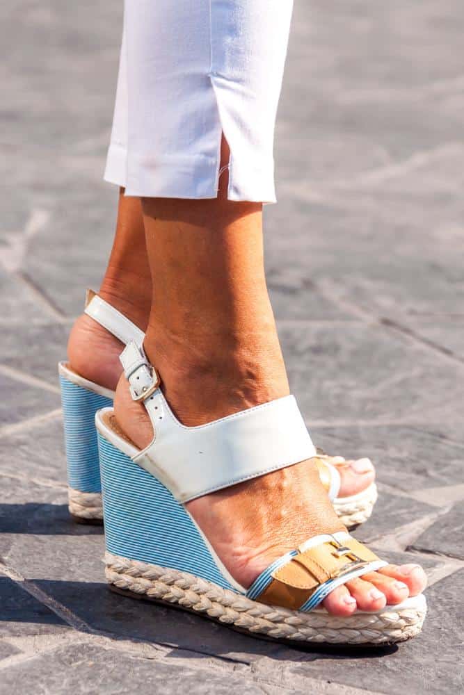 Woman's feet in blue and white wedges on tiled pavement