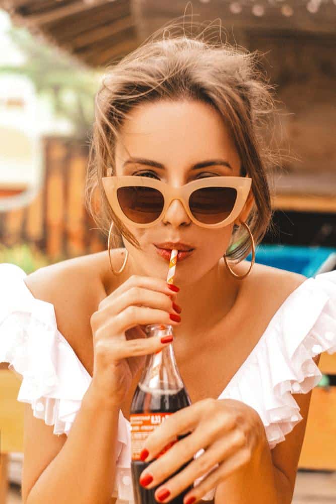 Girl wearing brown sunglasses while drinking a Coca Cola through a straw