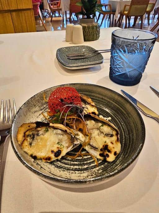 oysters rockefeller next to a blue cup and silverware on a white tableclothed table in a restaurant