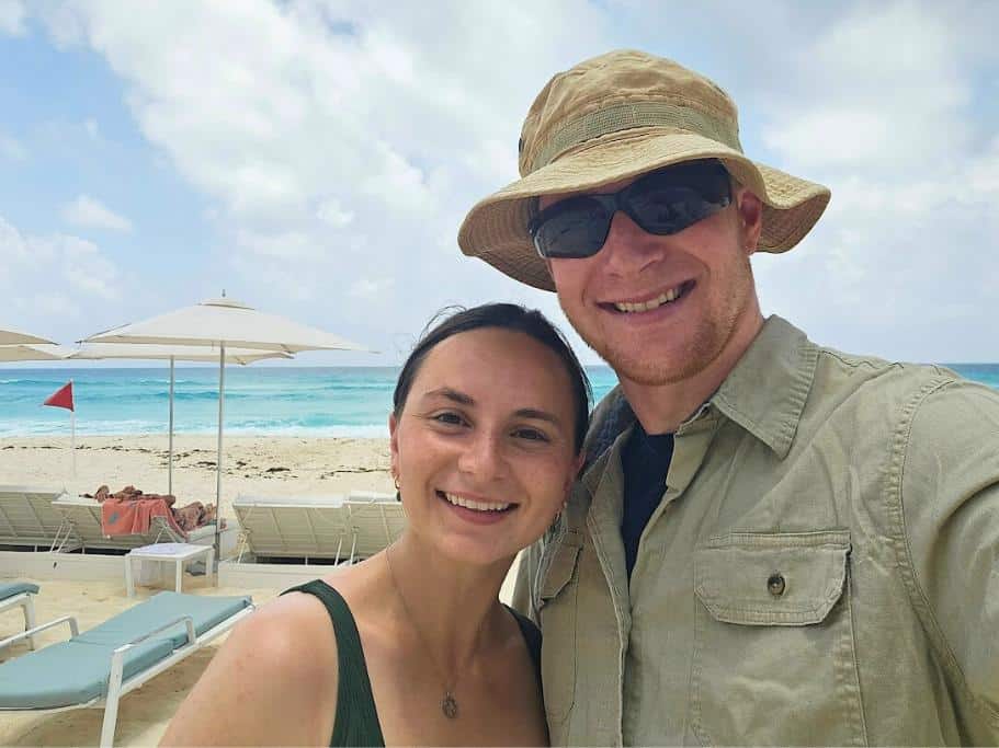Man and woman smiling on a beach with chairs and umbrellas