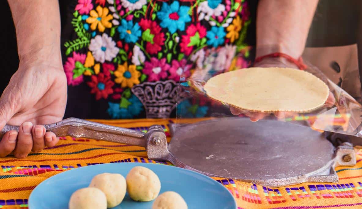Woman in a colorful dress pressing homemade corn tortillas with a traditional press