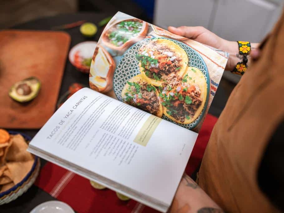 Person holding a cookbook with a recipe for tacos on the page