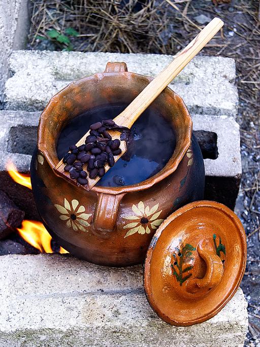 Clay pot with sunflowers painted on the side and a wooden spoon with black beans