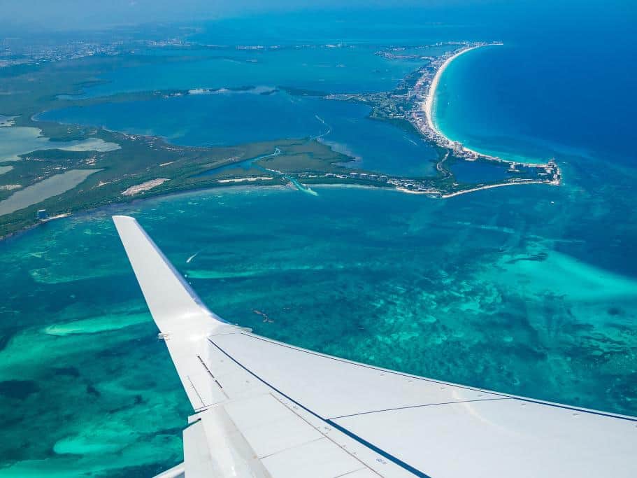 Airplane wing above the ocean with long peninsula