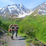 Two hikers on a rocky trail surrounded by mountains