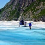 Person approaching a landing helicopter on a blue and white glacier