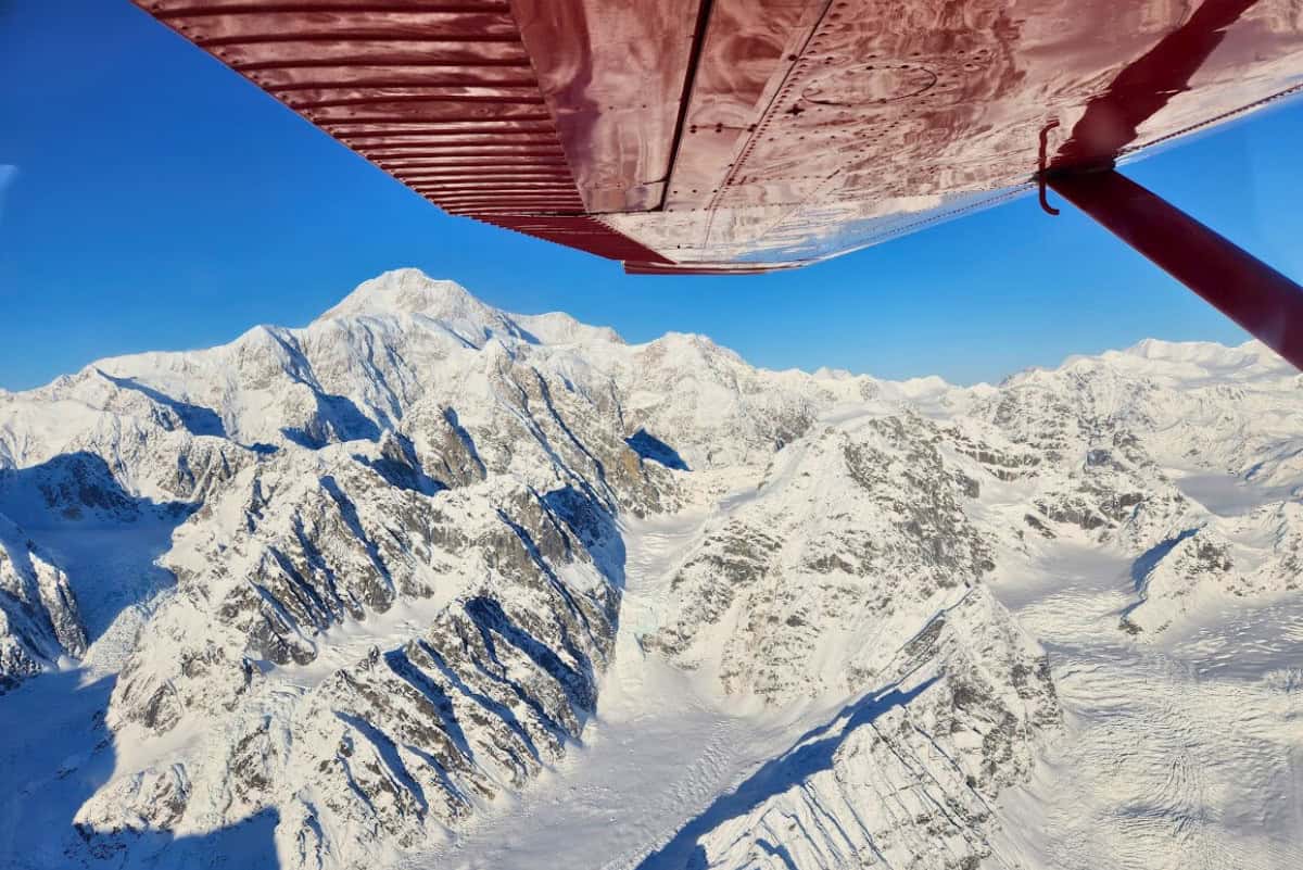 Red wing of a small airplane overlooking snowy mountains and glaciers