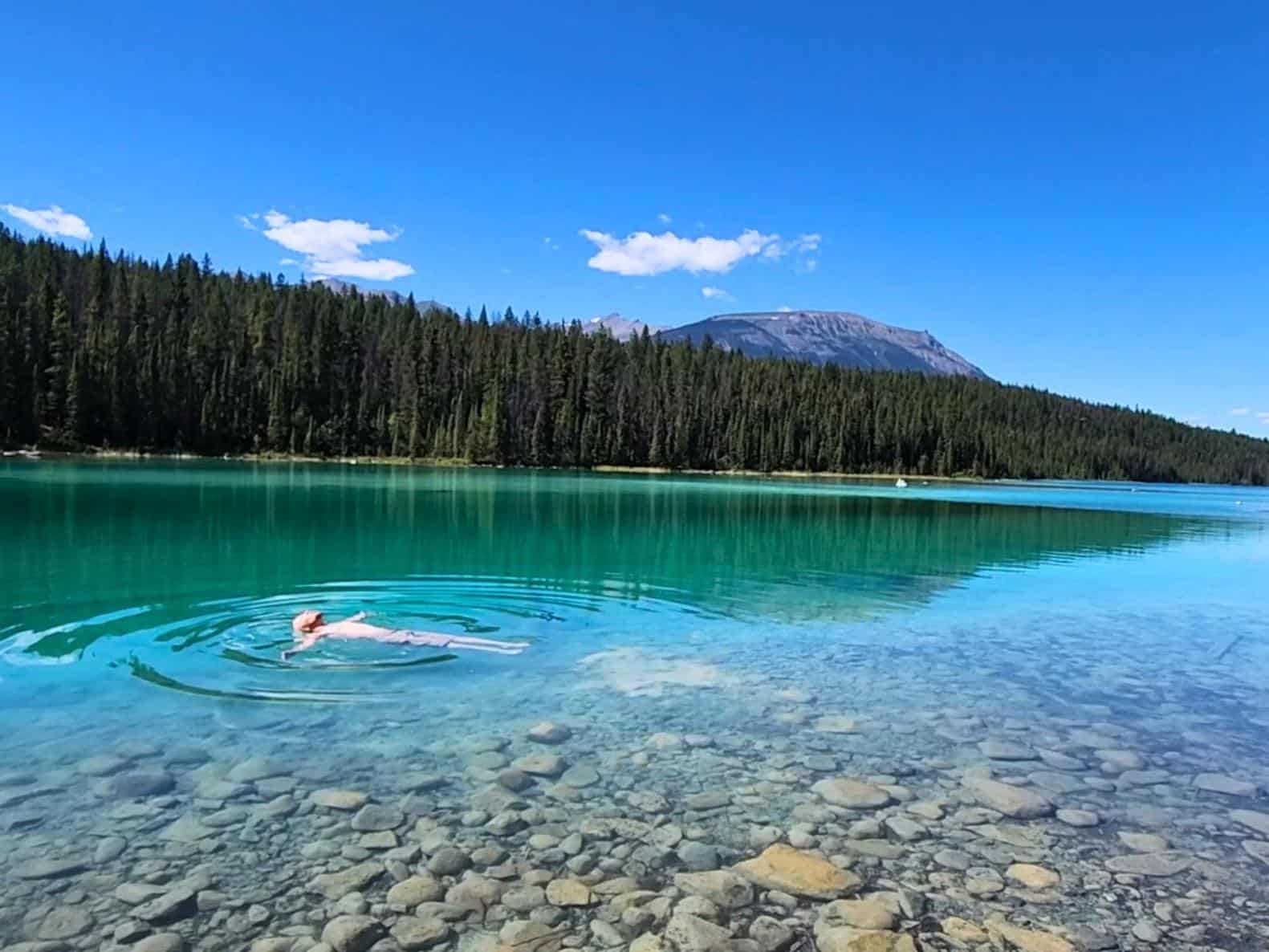 Person floating no their back in clear, turquoise water in Jasper National Park