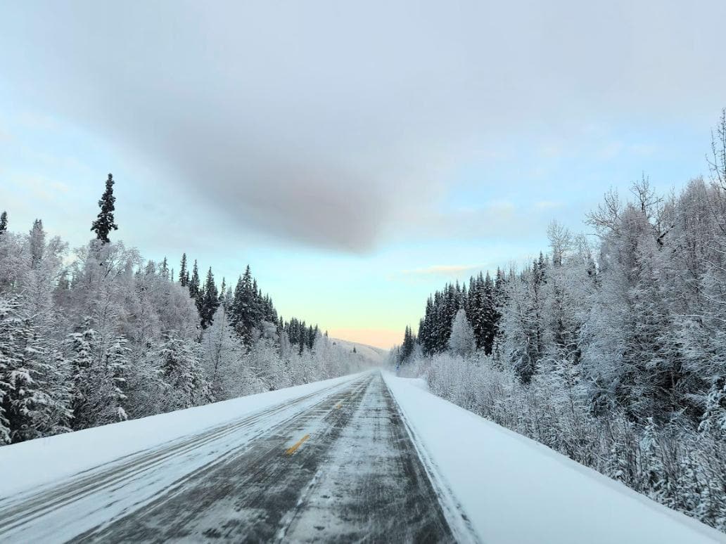 Icy road surrounded by snow and snowy trees on a bright day in Fairbanks, AK