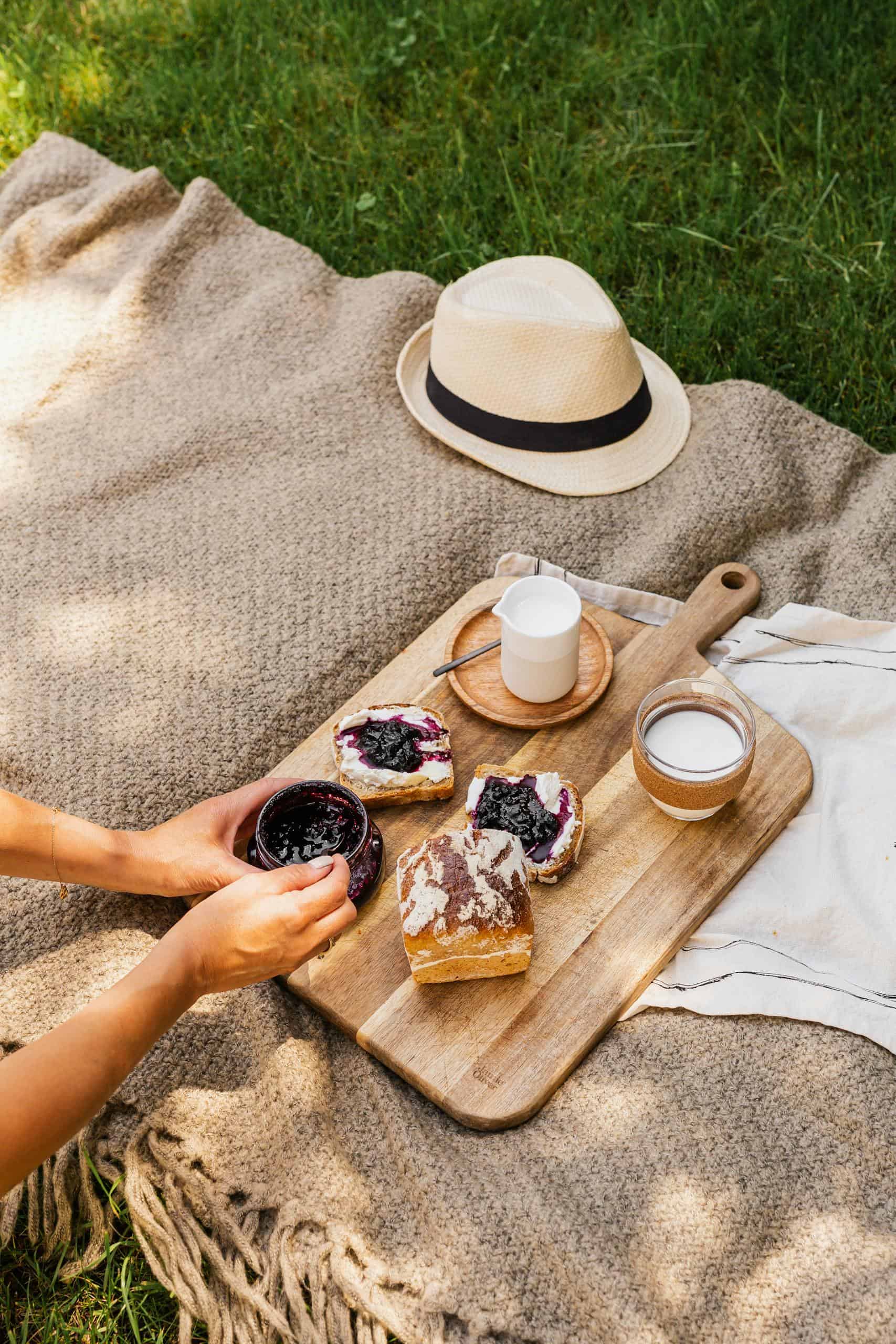 A cozy outdoor picnic with bread, jam, and milk on a blanket, styled for a serene breakfast setting.