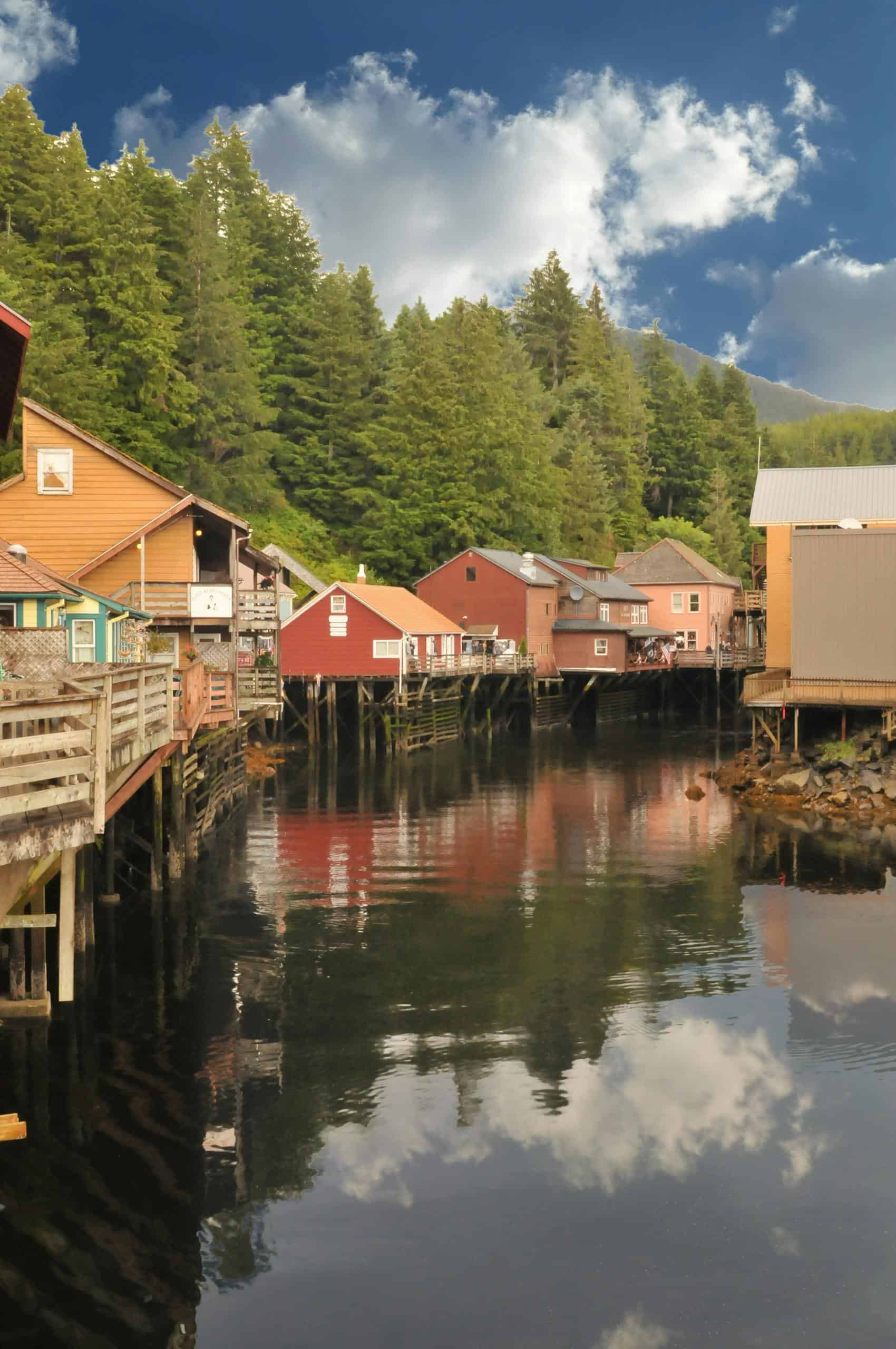 Picturesque stilt houses along a forested river, reflecting the serene summer sky.