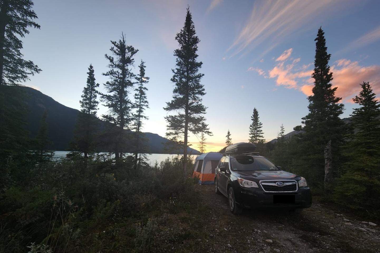 A car parked in front of a tent on Muncho Lake in BC, Canada at sunset