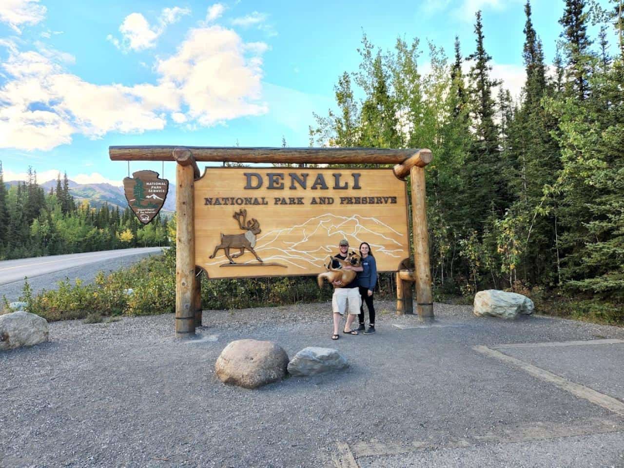 Sean and Emily Concannon standing in front of the Denali National Park sign with their dog