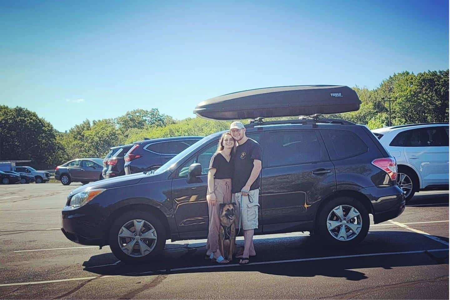 Sean and Emily Concannon standing in front of their SUV with their dog in a parking lot