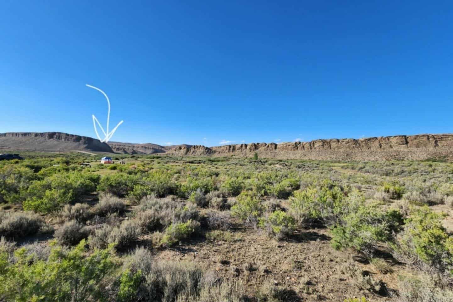A wide view of an open valley in the desert surrounded by mountains in Montana with a white arrow pointing to a tent in the middle