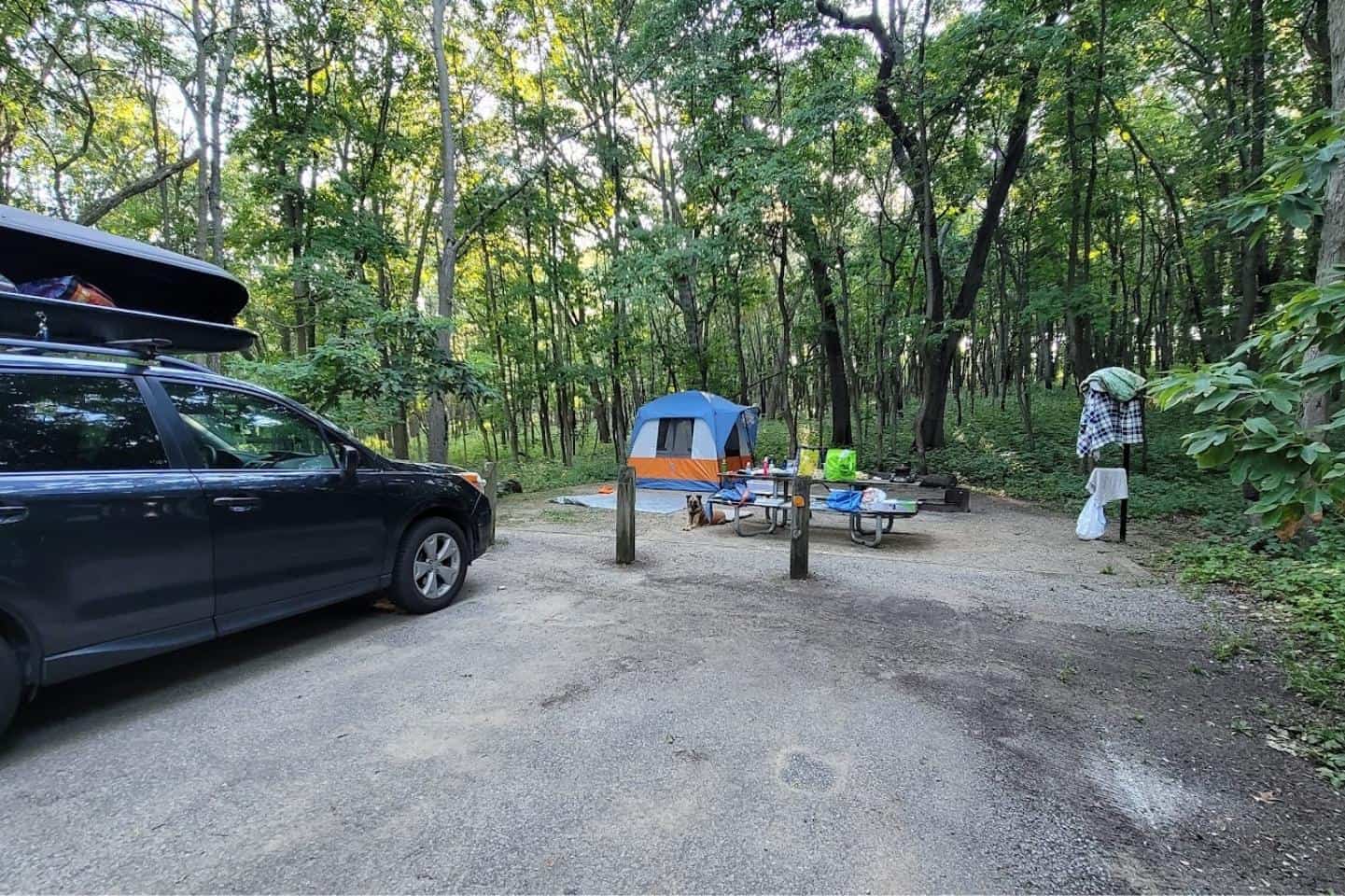 A basic campsite with a car, tent, picnic table, and fire ring on gravel
