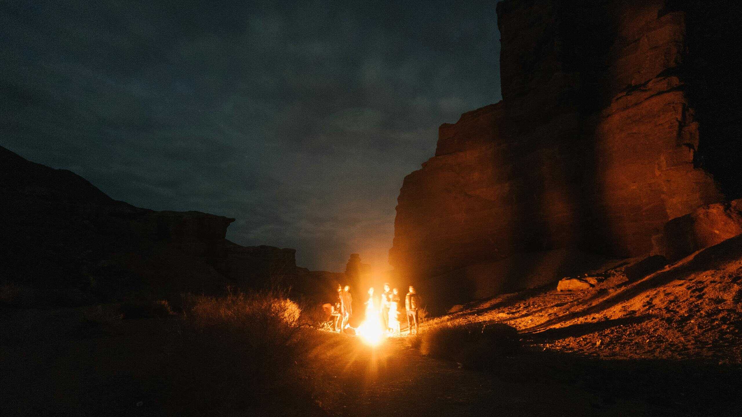 A serene campfire gathering at Charyn Canyon, Almaty Province captured at night, showcasing natural shadows and silhouettes.