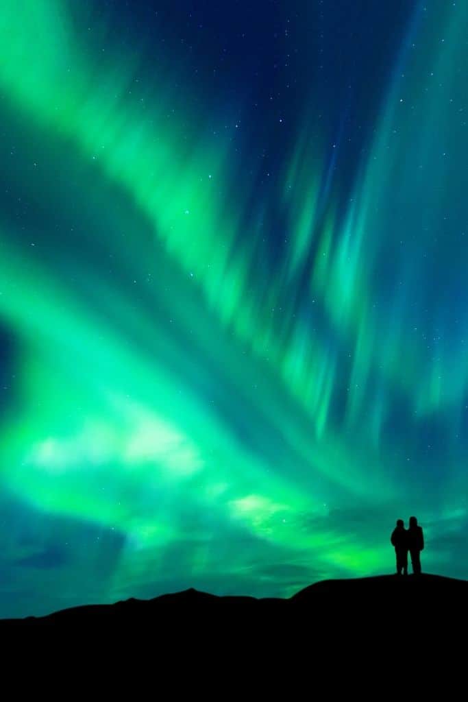 Black silhouette of two people standing under the northern lights